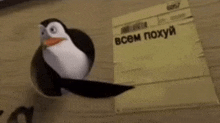 a penguin is sitting on a wooden table next to a piece of paper with russian writing on it .