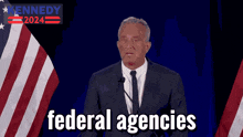 a man in a suit and tie stands in front of a microphone with the words federal agencies in front of him