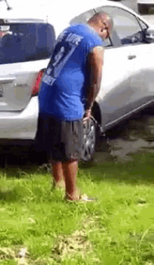 a man in a blue shirt is standing in front of a white car .