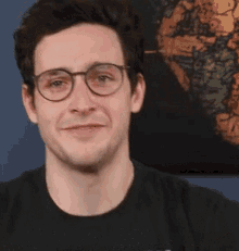 a man wearing glasses and a black shirt is smiling in front of a painting .