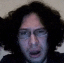 a man with curly hair and glasses is making a face .