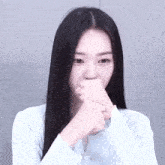 a woman with long black hair is covering her mouth with her hands