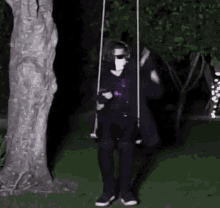 a man in a mask is sitting on a swing in front of a tree .