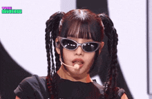 a woman wearing pigtails and sunglasses is singing into a microphone .