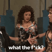 a woman in a floral dress is pointing at another woman and the words what the f * ck are on the screen
