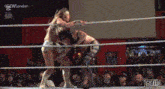 two women are wrestling in a ring with a crowd watching .