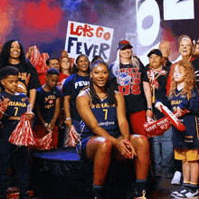 a woman sitting in front of a sign that says " let 's go fever "