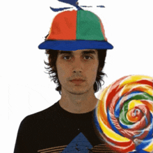 a man wearing a colorful hat is holding a large lollipop