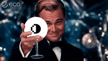 a man in a tuxedo is holding a cd with the letter d on it in front of an eco logo