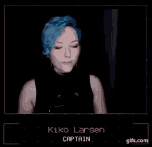 a woman with blue hair is wearing a black tank top and standing in a dark room .