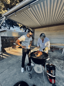 a man and a woman cooking on a grill with a bag of kingsford charcoal nearby