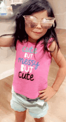 a little girl is wearing sunglasses and a pink shirt that says cute but messy but cute