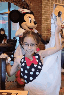 a little girl in a polka dot dress is posing for a photo with minnie mouse