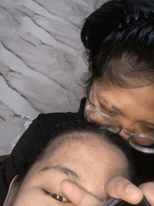 a woman wearing glasses is applying makeup to another woman 's eyebrows