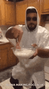 a man wearing a hooded jacket and sunglasses is mixing something in a bowl in a kitchen .