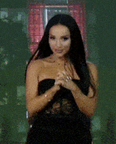 a woman in a black dress is standing in front of a window with her hands folded