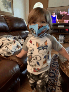 a young boy wearing a mask and a shirt with a pig on it stands in front of a couch