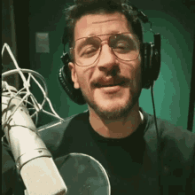 a man wearing glasses and headphones stands in front of a microphone