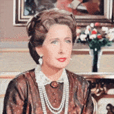 a woman wearing a pearl necklace and earrings is sitting in front of a vase of flowers