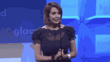 a woman in a black dress stands in front of a microphone in front of a blue wall that says glaad