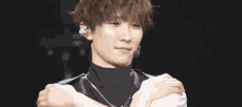 a young man wearing a black turtleneck and a necklace holds his arm over his shoulder