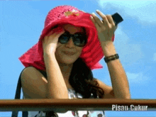 a woman wearing a pink hat and sunglasses has the word pisau written on the bottom