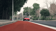 a red sports car is driving down a road with trees on the side