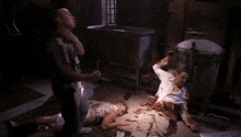 a group of people are standing around a man laying on the floor covered in blood .