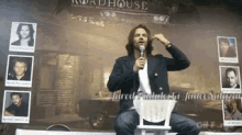 a man speaking into a microphone in front of a wall that says roadhouse