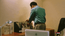 a man in a blue shirt is standing in front of a desk with an apple laptop and a full logo on the bottom right