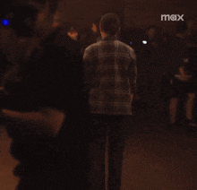 a man in a plaid shirt stands in front of a crowd with the word max on the bottom left