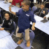 a boy wearing a blue shirt with the word eagle on it is standing on a chair