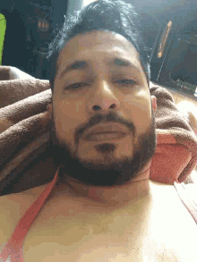 a man with a beard is laying on a bed with a towel around his neck