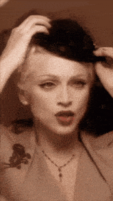 a woman wearing a hat and a necklace looks at herself in a mirror