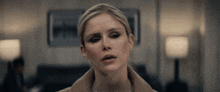 a woman in a brown coat looks at the camera