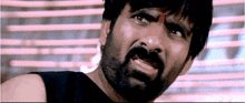 a man with a beard and a red circle on his forehead looks at the camera