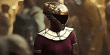 a woman is wearing a gold helmet and a red costume .