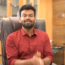 a man in a red shirt is sitting in a chair and smiling