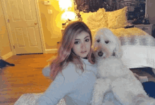 a girl with pink hair holds a small white dog in front of a bed