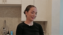 a young woman is standing in a kitchen next to a sink and smiling .