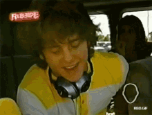 a man wearing headphones is sitting in the back seat of a car with a rebelpe sign above his head