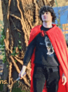 a man in a red cape is holding a knife in front of a tree