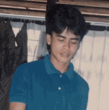a young man in a blue polo shirt is standing in front of a window .