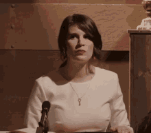 a woman wearing a key necklace sits at a table with a microphone