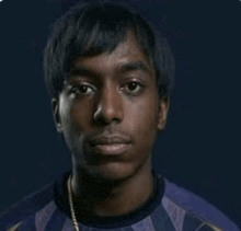 a young man wearing a purple shirt and a gold chain is looking at the camera with a dark background .