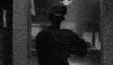 a black and white photo of a woman walking down a dark alleyway holding an umbrella .