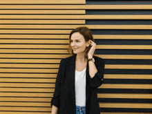 a woman wearing a black jacket and a white shirt stands in front of a wooden wall