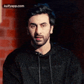 a man with a beard and a black hoodie is making a funny face .
