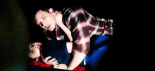 a man in a plaid shirt is laying on top of a woman in a dark room .