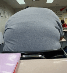 a man sits at a desk in a classroom with a binder on the desk